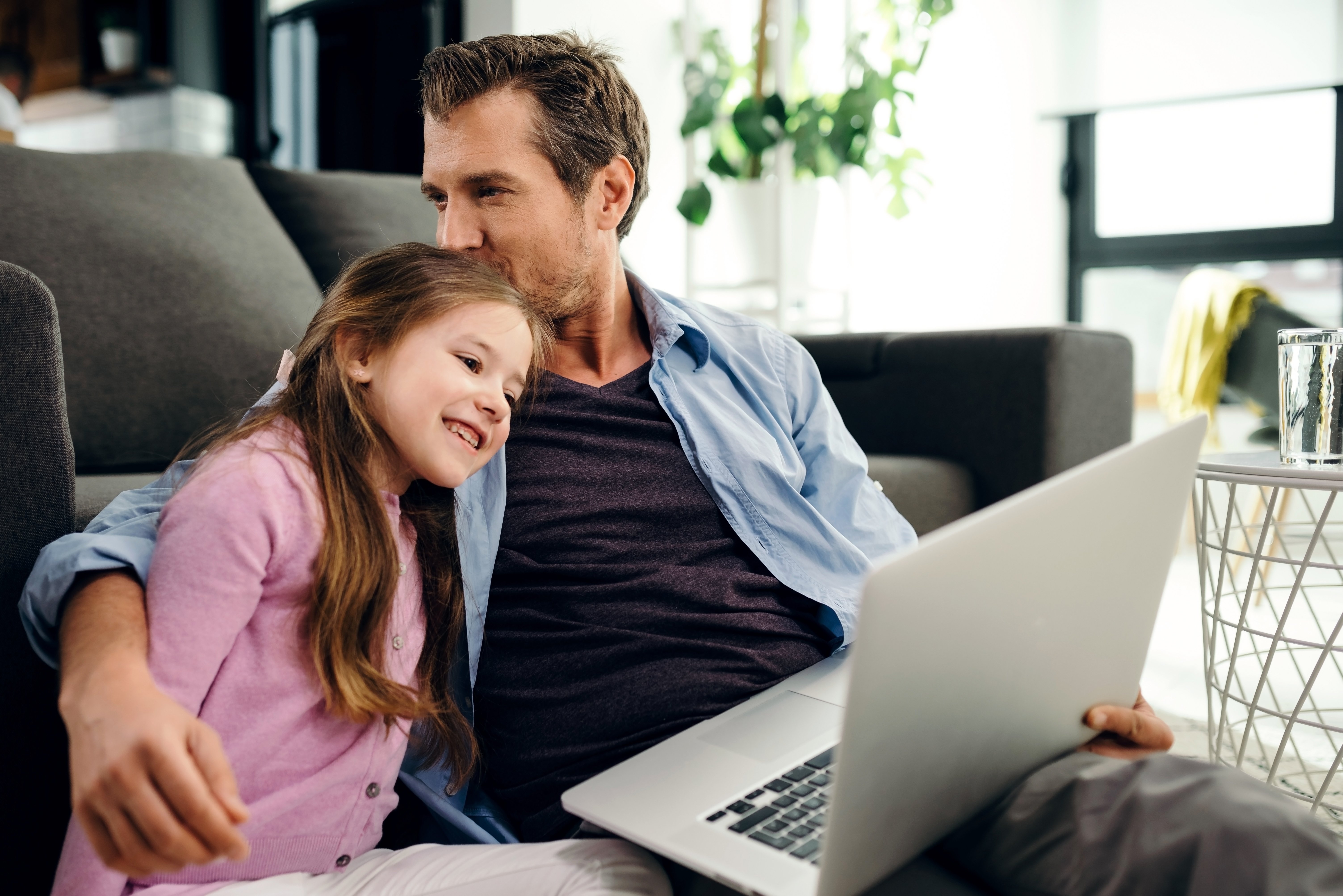 affectionate-father-giving-kiss-his-daughter-while-using-computer-relaxing-living-room